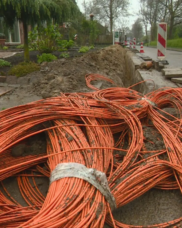 Oranje glasvezelbuizen naast een open sleuf in een woonstraat