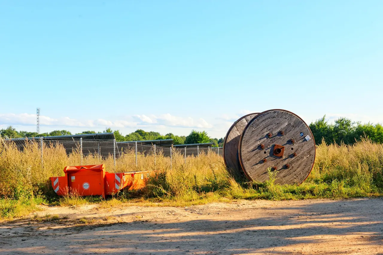 Houten kabelhaspel en oranje afzetbakken op een werkterrein naast een zonnepark