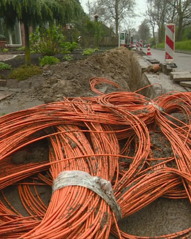Oranje glasvezelbuizen naast een open sleuf in een woonstraat